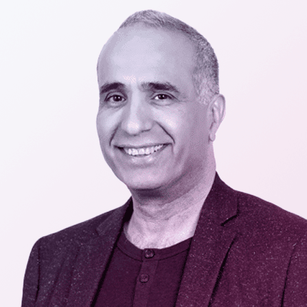 A middle-aged man with short gray hair, smiling, wearing a blazer over a dark shirt, posed against a light background.