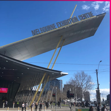 The Melbourne Exhibition Centre features a large, slanted roof with its name displayed on top; people walk outside under a partly cloudy sky during Memcyco at CyberCon Australia 2025.